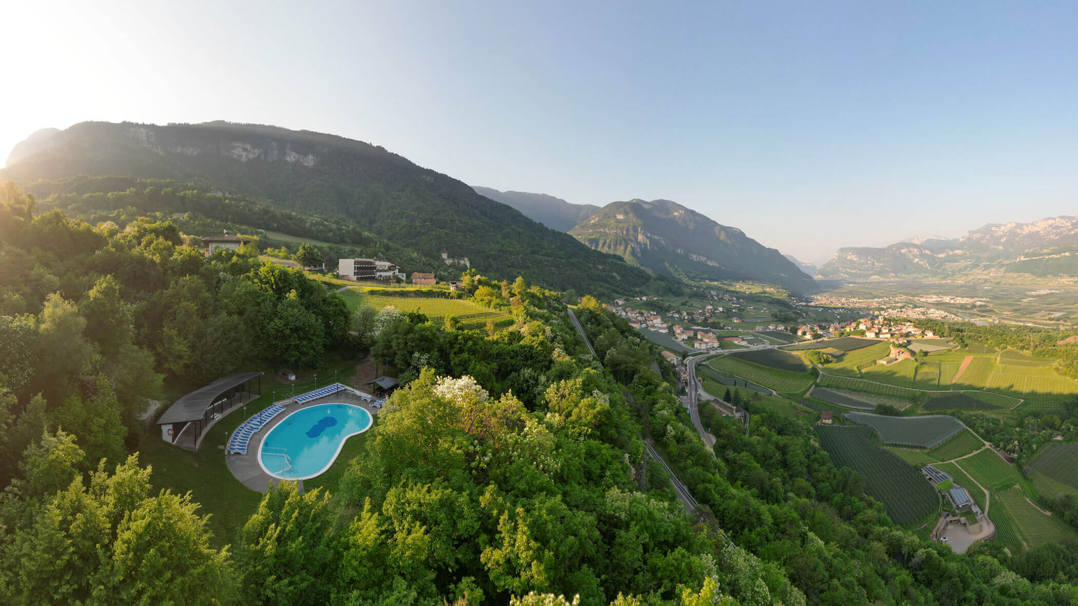 Luftaufnahme eines Pools auf einem Hügel, grüne Weinberge und Berge unter einem klaren blauen Himmel. - Hotel Tenz